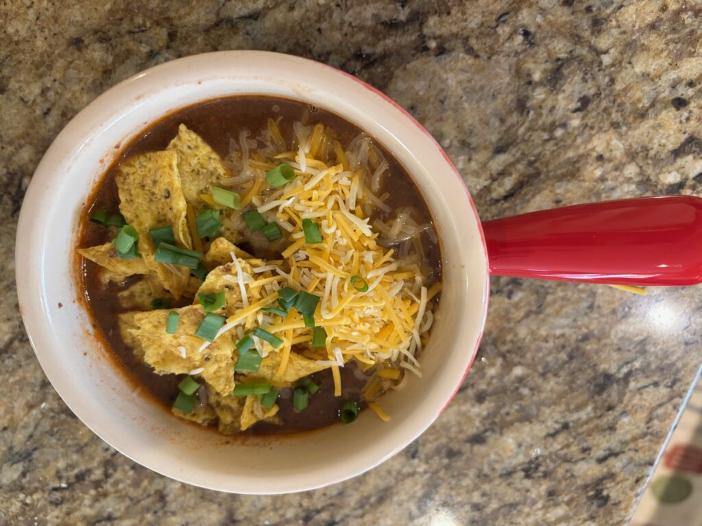 This is a picture of the finished black bean soup in a bowl with garnishes tortilla chips, cheddar cheese and scallions.
